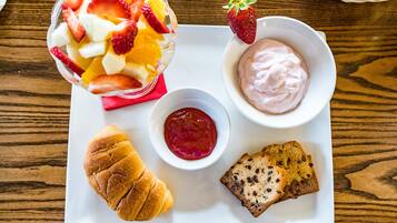 A tray with a fruit salad, yogurt, jam, a croissant, and a slice of bread.