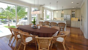 Een ruime keuken met witte kasten, een groot eiland en een eethoek met rieten stoelen en een ronde tafel.