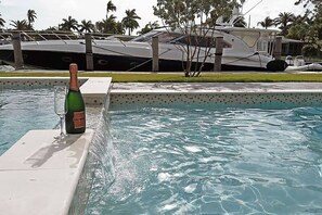 A pool with a bottle of champagne and a glass on the edge. - 6 Bedroom Homes in Miami by TMG (Miami)