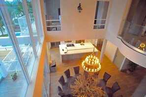 A modern kitchen with a central island, a dining area with a unique chandelier, and large windows offering a view of the outdoors. - 6 Bedroom Homes in Miami by TMG (Miami)