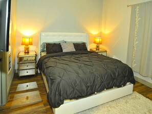 A bedroom with a large bed, two bedside tables with lamps, a white headboard, and a wooden floor. - 6 Bedroom Homes in Miami by TMG (Miami)