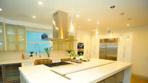 A modern kitchen with a large island, stainless steel appliances, and pendant lighting. - 6 Bedroom Homes in Miami by TMG (Miami)