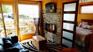 A cozy room with a sofa, a wooden table, a stone wall, a television, and a bed. - Cabañas Rincón Austral (Puerto Montt)