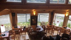 A cozy restaurant with wooden furniture, a central dining table, and large windows offering a view of the outdoors. - Cabañas Rincón Austral (Puerto Montt)