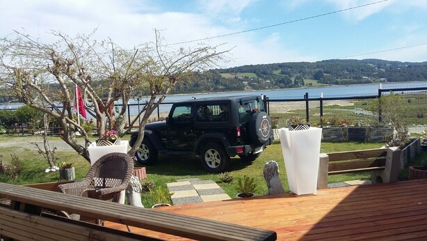 A deck with a black SUV parked nearby, surrounded by outdoor furniture and a view of a lake and hills. - Cabañas Rincón Austral (Puerto Montt)