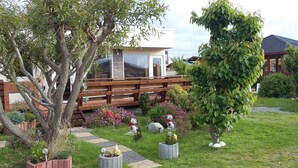 A garden with a wooden deck, various plants, and a white building with large windows. - Cabañas Rincón Austral (Puerto Montt)