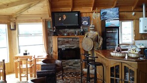 A cozy cabin interior with a stone fireplace, wooden furniture, and a mounted television. - Cabañas Rincón Austral (Puerto Montt)
