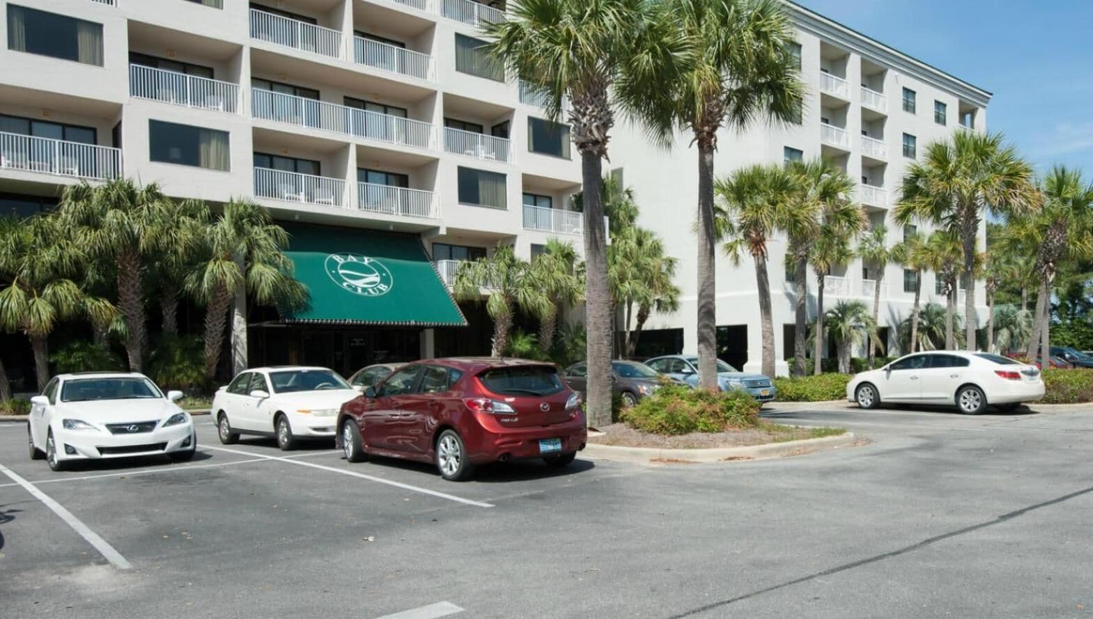 Un hotel con toldo verde y un estacionamiento con varios coches.
