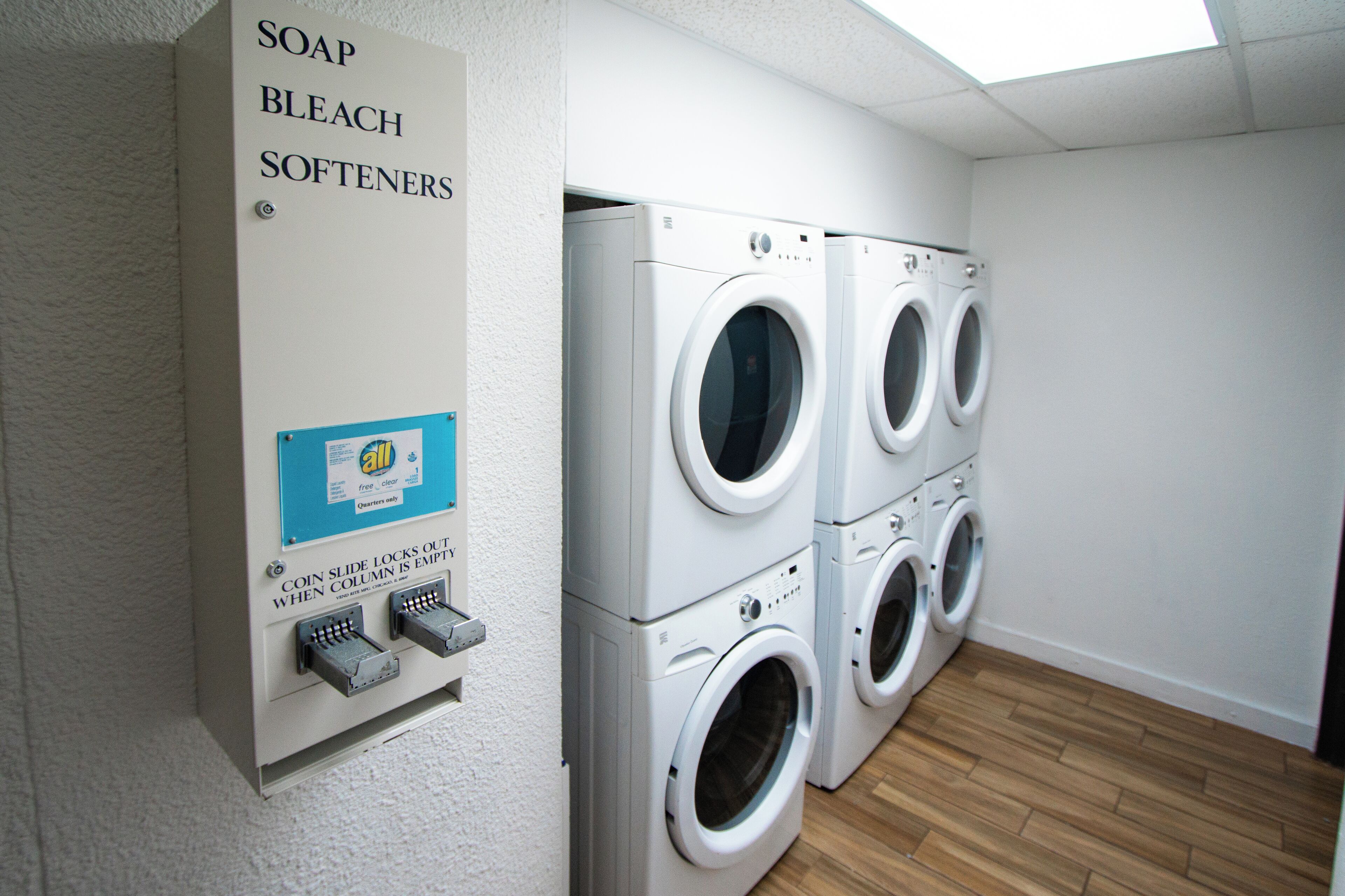 A laundry area with a sign listing soap, bleach, and softeners, and a coin-operated washer and dryer.