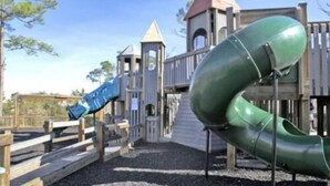 Un parque infantil con tobogán, estructura para escalar y una pequeña torre.