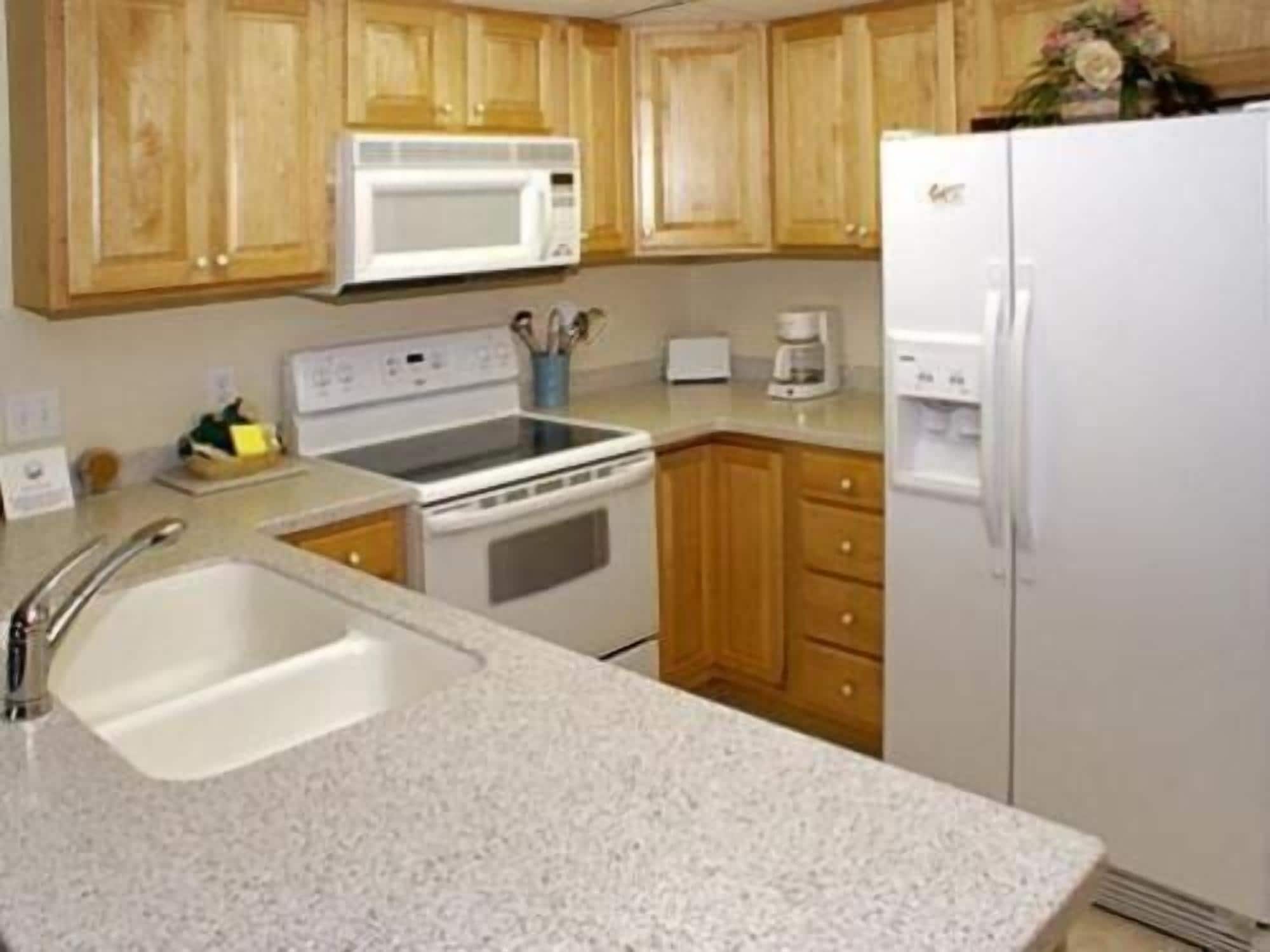 A kitchen with wooden cabinets, a white microwave, a stove, a sink, and a refrigerator.