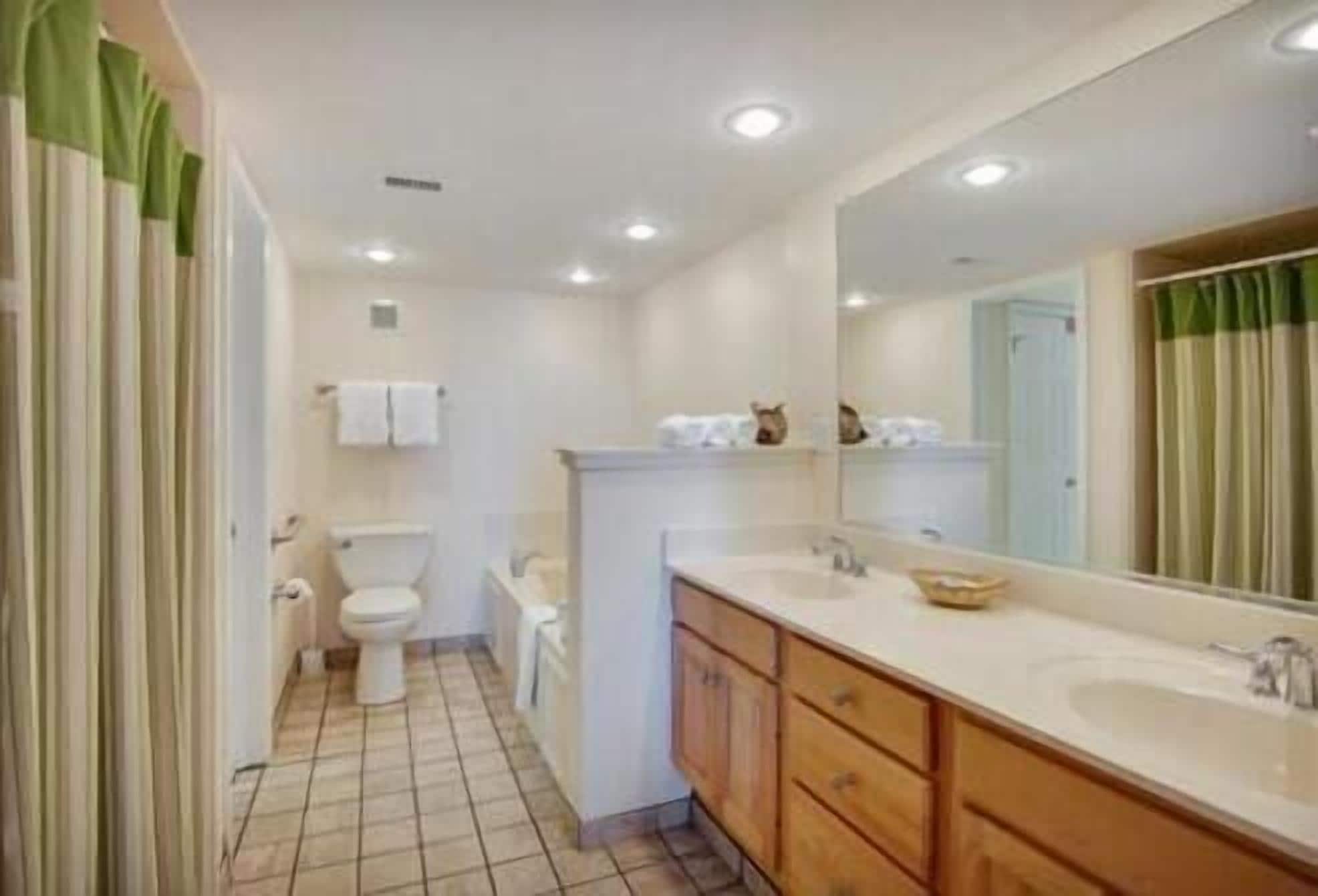 A bathroom with a large mirror, two sinks, a toilet, and a shower area.