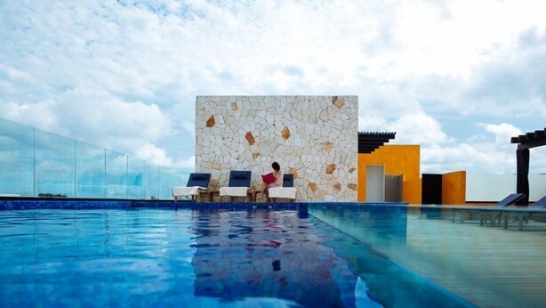A modern outdoor swimming pool with clear blue water, lounge chairs, and a stone wall with a geometric pattern. - Trendy 2BR condo centermost by Happy Address (Playa del Carmen)