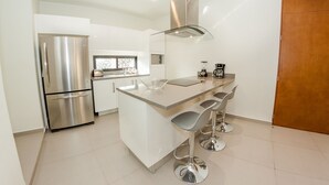 A modern kitchen with a stainless steel refrigerator, a built-in island with bar stools, and a coffee maker. - Trendy 2BR condo centermost by Happy Address (Playa del Carmen)