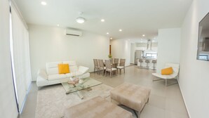 A modern living room with a sofa, ottomans, a coffee table, and a dining area with chairs and a table. - Trendy 2BR condo centermost by Happy Address (Playa del Carmen)