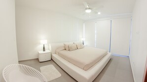 A modern bedroom with a large bed, a bedside table with a lamp, a ceiling fan, and a view of the outdoors through large windows. - Trendy 2BR condo centermost by Happy Address (Playa del Carmen)