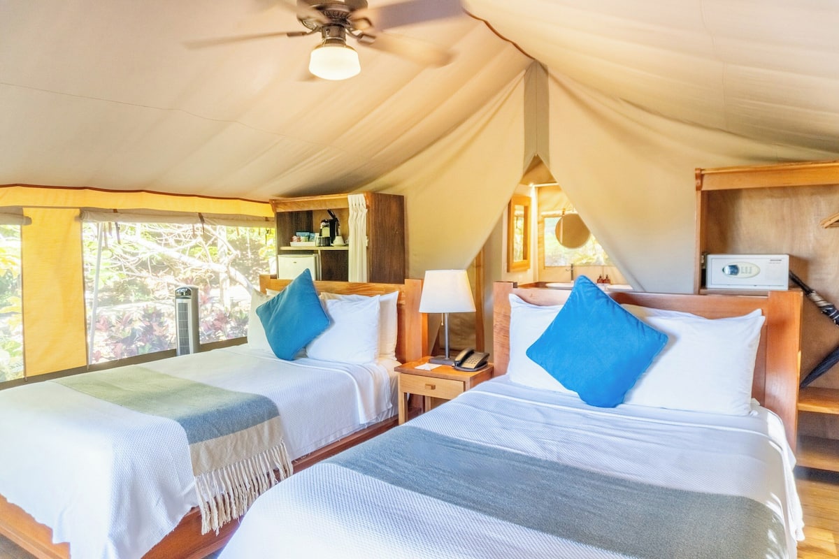 A tent-style room with two beds, each with a nightstand, a lamp, and a telephone.