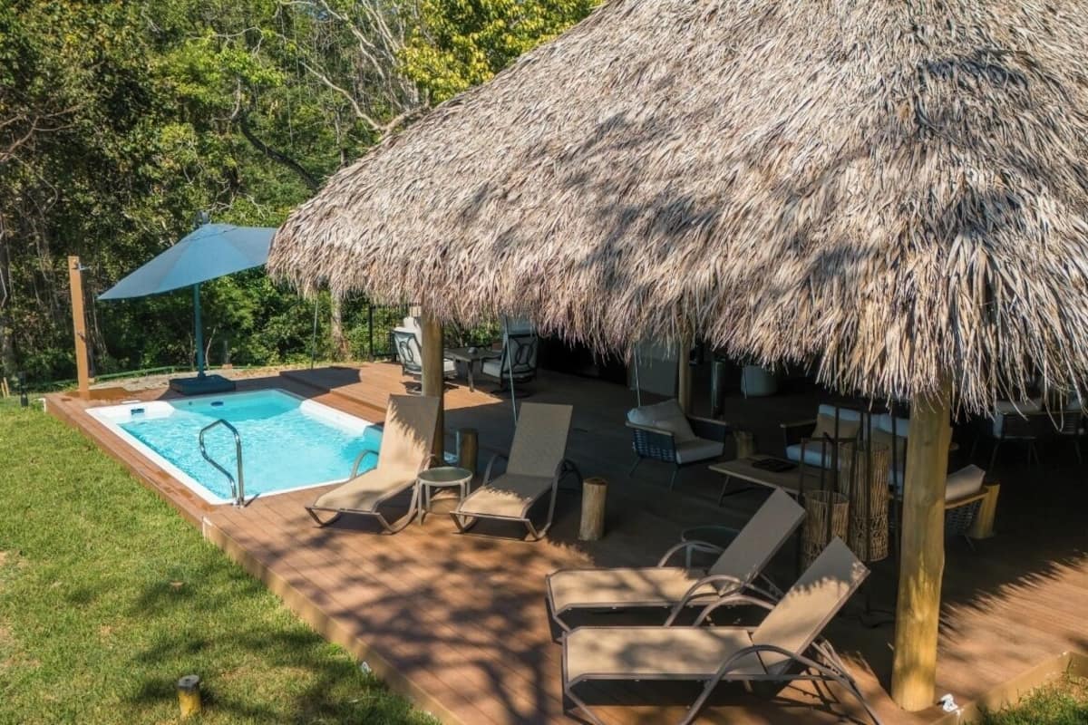A pool area with lounge chairs and a thatched roof structure.
