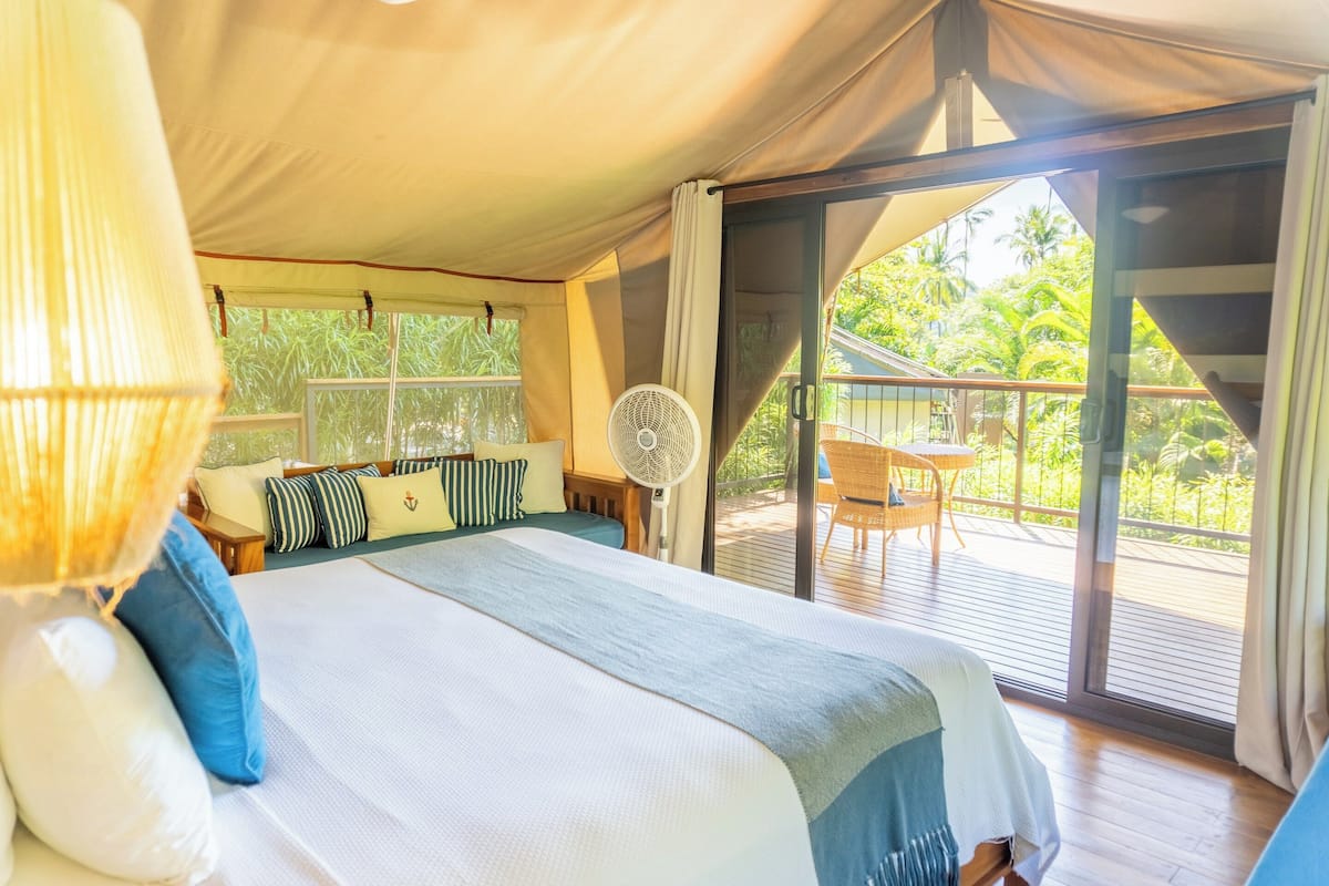 A bedroom with a bed, pillows, a fan, and a view of the outdoors.