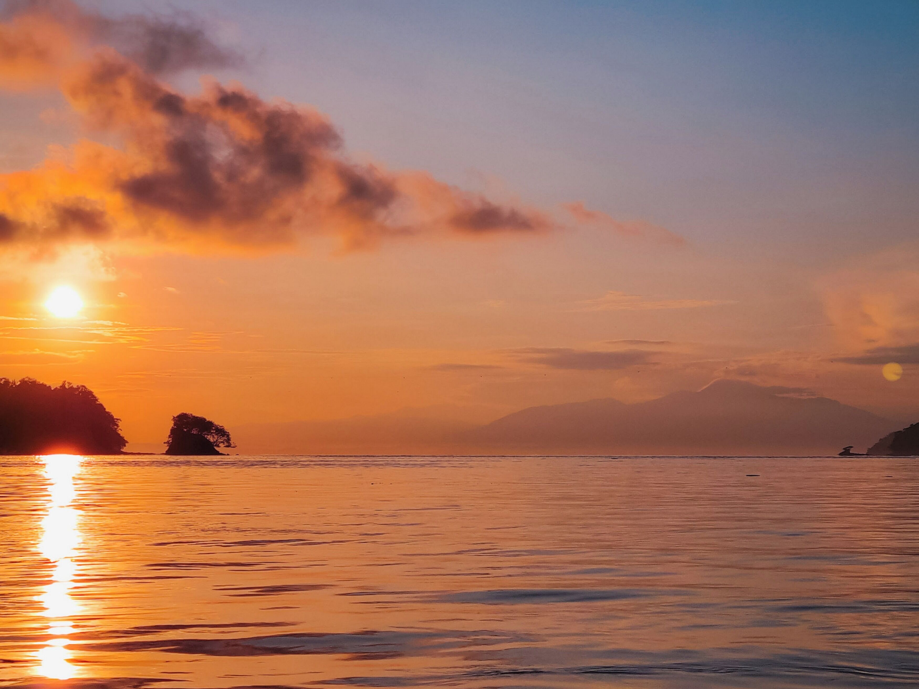 A sunset over a calm body of water with distant landforms.