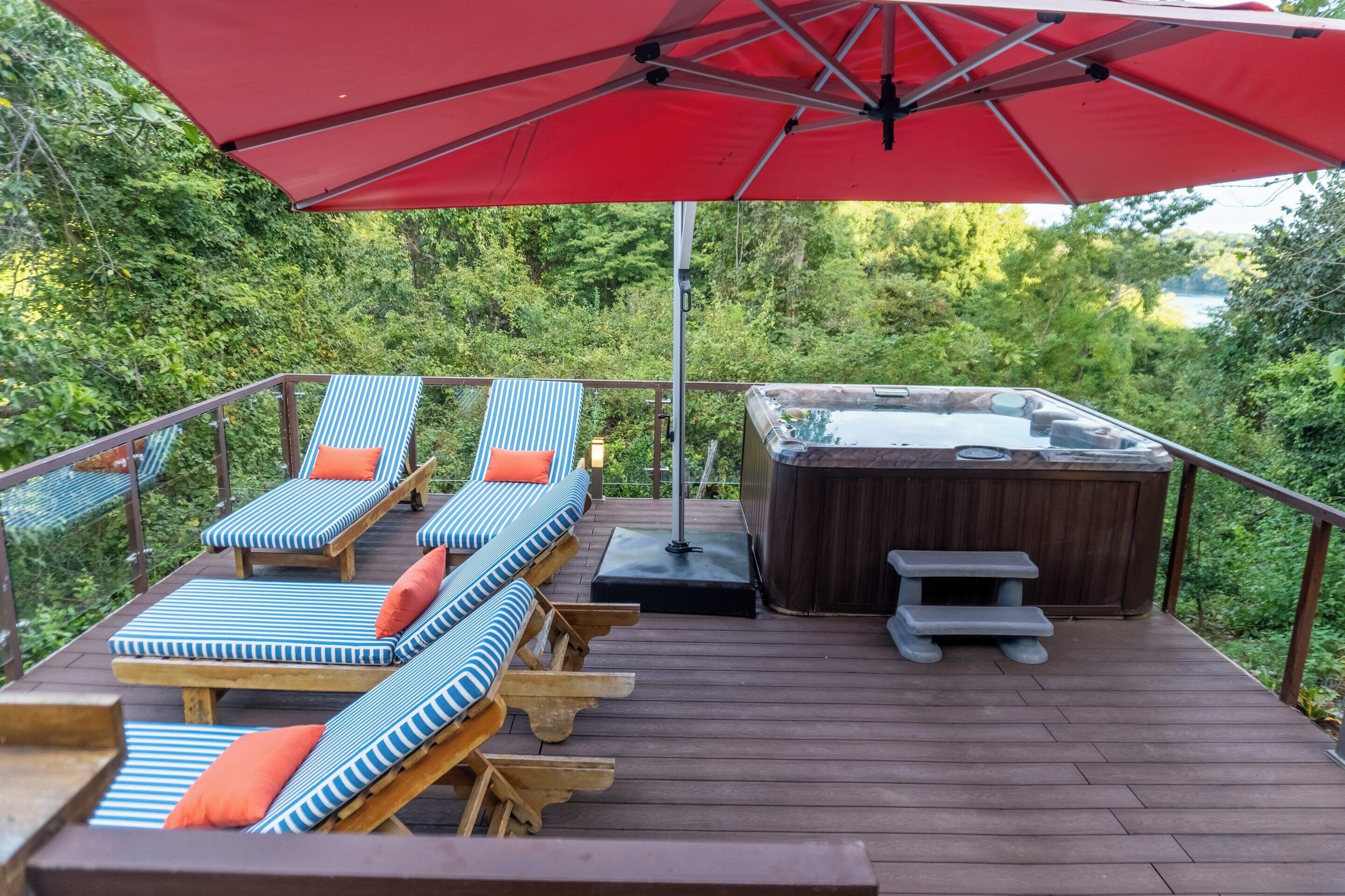 A deck with lounge chairs, a hot tub, and a table under a red umbrella.