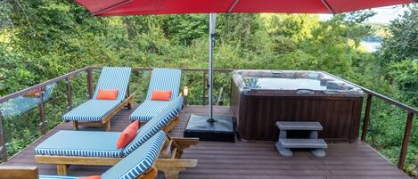 A deck with lounge chairs, a hot tub, and a table under a red umbrella.