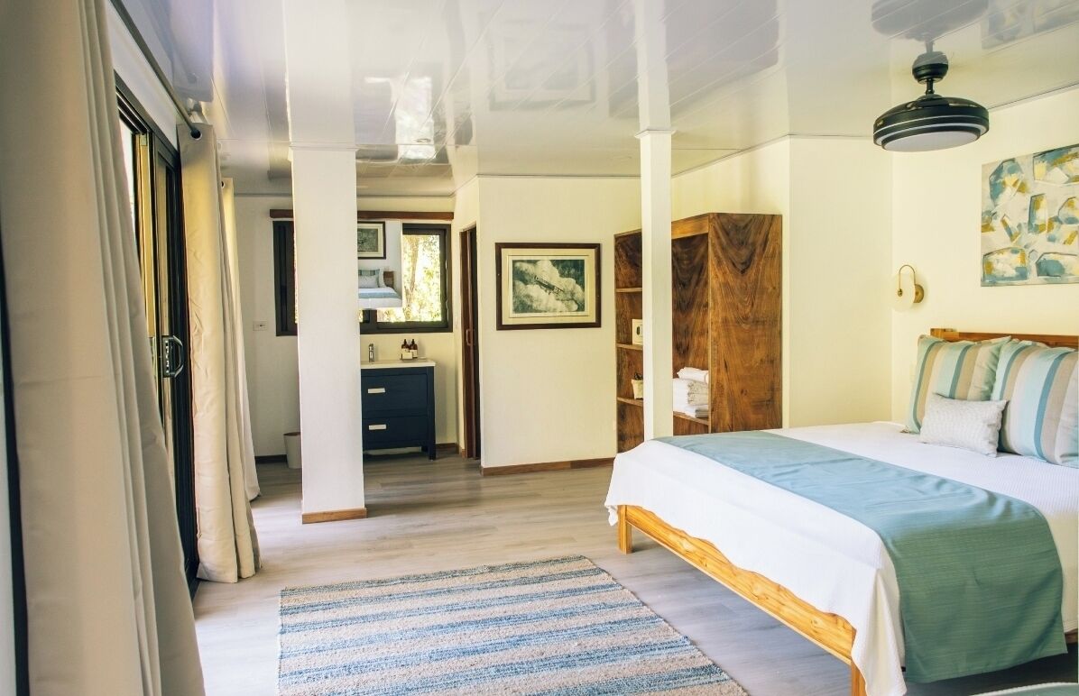A bedroom with a bed, a wooden wardrobe, a desk, and a window.
