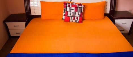 A bed with an orange and blue bedspread, a patterned pillow, and a headboard with a light fixture.