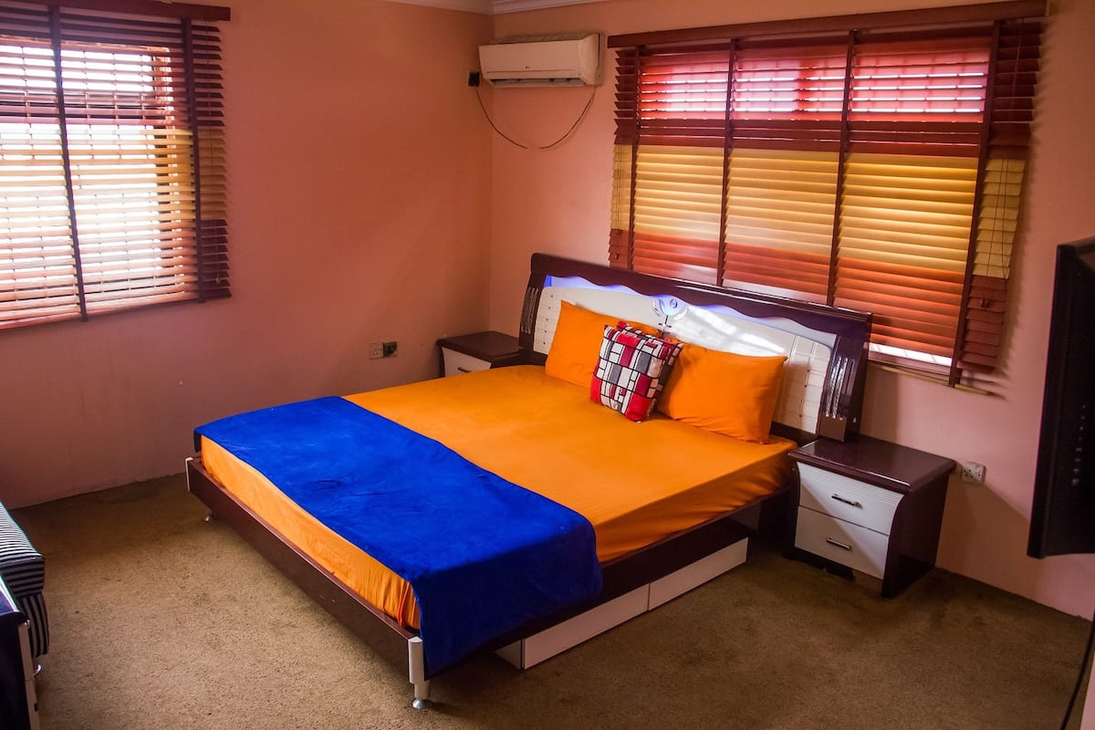 A bedroom with a bed, nightstands, a desk, and a window with blinds.