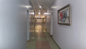 A long, narrow hallway with a tiled floor, a ceiling with recessed lighting, and a framed abstract painting on the right wall. - Dilic Hotel (Abuja)