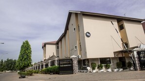 A building with a beige facade, a black gate, and a sign with "DH" on it. - Dilic Hotel (Abuja)