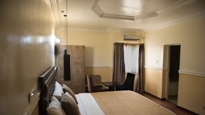 A hotel room with a large bed, a desk, a chair, and an air conditioning unit. - Dilic Hotel (Abuja)