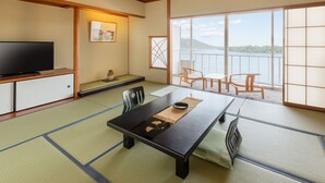 A traditional Japanese room with tatami flooring, a low table with a black mat, a television on a cabinet, and a view of a lake through large windows. - Amanohashidate Hotel (Miyazu)