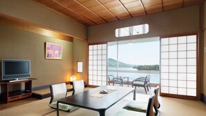 A traditional Japanese-style room with tatami flooring, a low table, and chairs. A television is placed on a wooden stand against the wall. - Amanohashidate Hotel (Miyazu)
