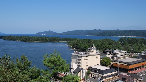 A coastal town with buildings near the water, a clear sky, and distant mountains. - Amanohashidate Hotel (Miyazu)