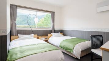 Une chambre d’hôtel avec deux lits, un bureau et une vue sur la verdure par la fenêtre.