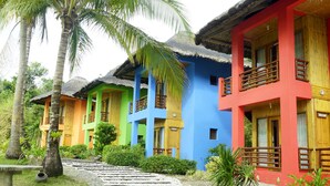 Una hilera de edificios coloridos con techos de paja, rodeados de palmeras y un sendero de piedra.