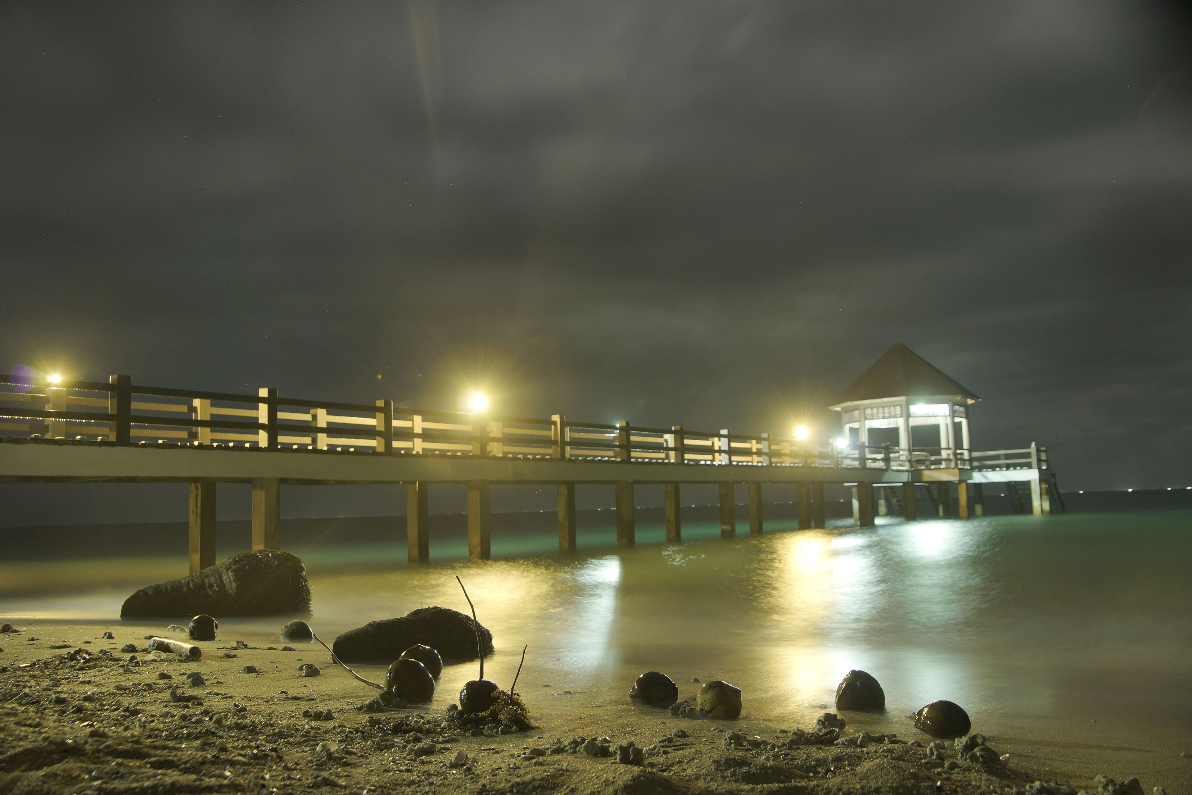 Un muelle se adentra en aguas tranquilas de noche, con un pequeño pabellón al final.