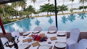 Mesa preparada para comer con vista a una piscina y palmeras.