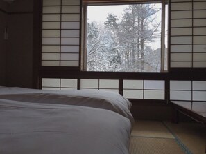 A traditional Japanese room with tatami flooring, a bed, and a window with a view of snow-covered trees. - Hakuba Landmark Happo Lodge (Hakuba)