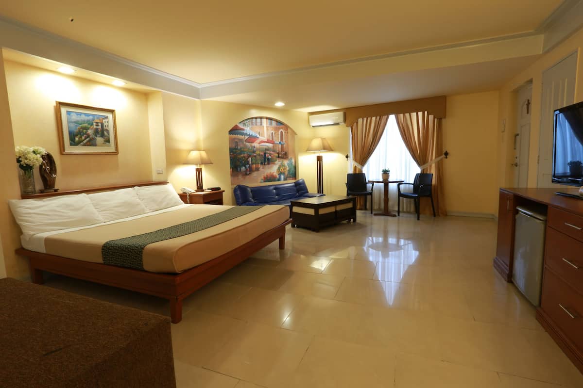 A hotel room with a large bed, a desk with a chair, a television, and a dining area with a table and chairs.