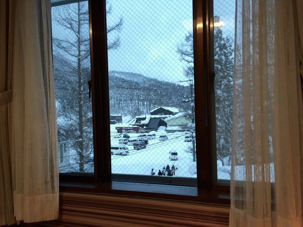 Ein Fenster mit Blick auf eine verschneite Straße, ein Gebäude mit einem Schild und kahl stehende Bäume.