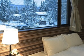 Habitación de hotel con una cama, una lámpara de noche y una ventana con vistas a un paisaje nevado.