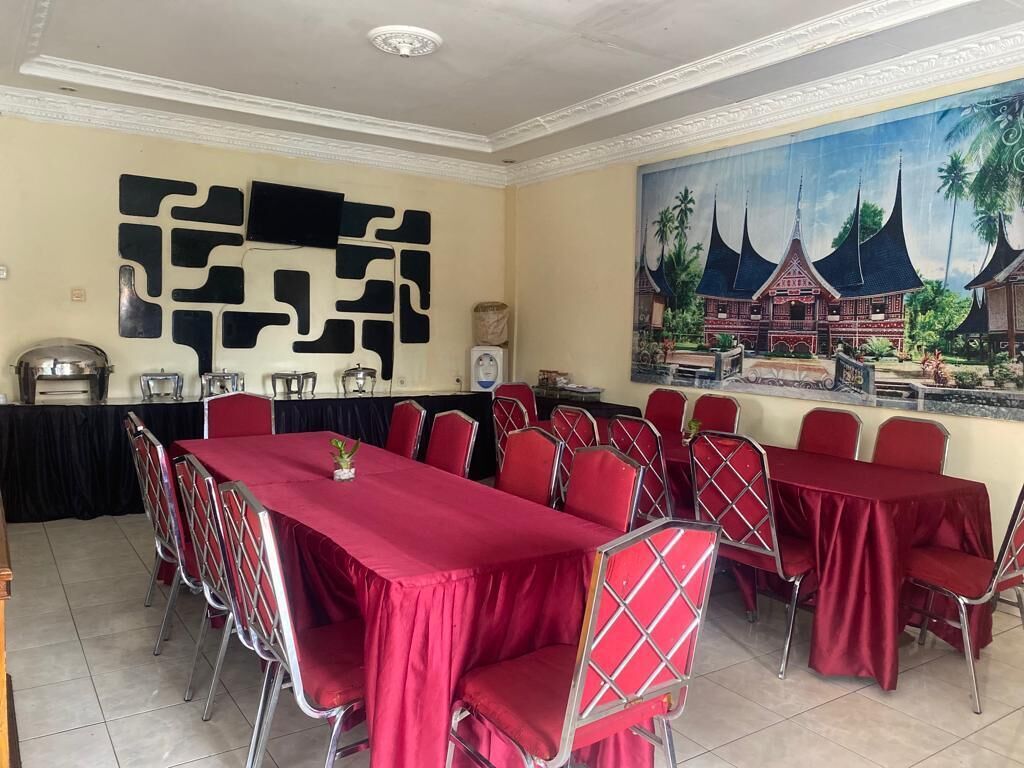 Een vergaderzaal met een lange tafel en rode stoelen, een groot schilderij van traditionele architectuur, en een decoratief wandobject.