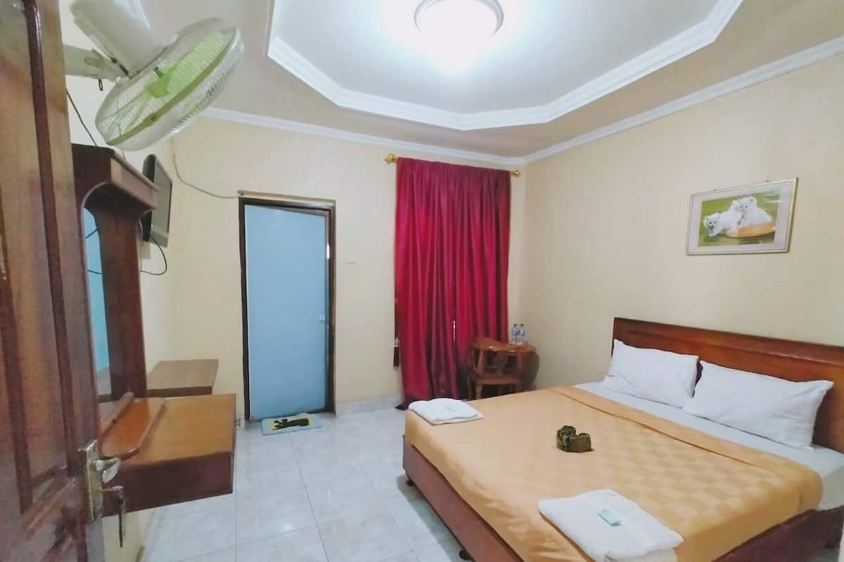 Habitación de hotel con cama, escritorio, silla, ventilador, puerta y cortina roja.