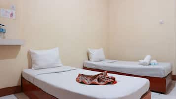 Una habitación de hotel con dos camas individuales, cada una con ropa de cama y almohadas blancas. Una manta estampada está colocada sobre la cama en primer plano.