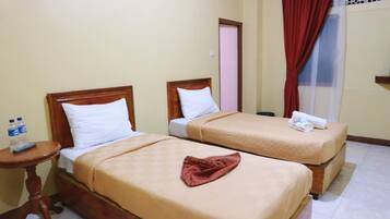Two single beds with wooden headboards, a small wooden table with a remote control, and a water bottle on the table.