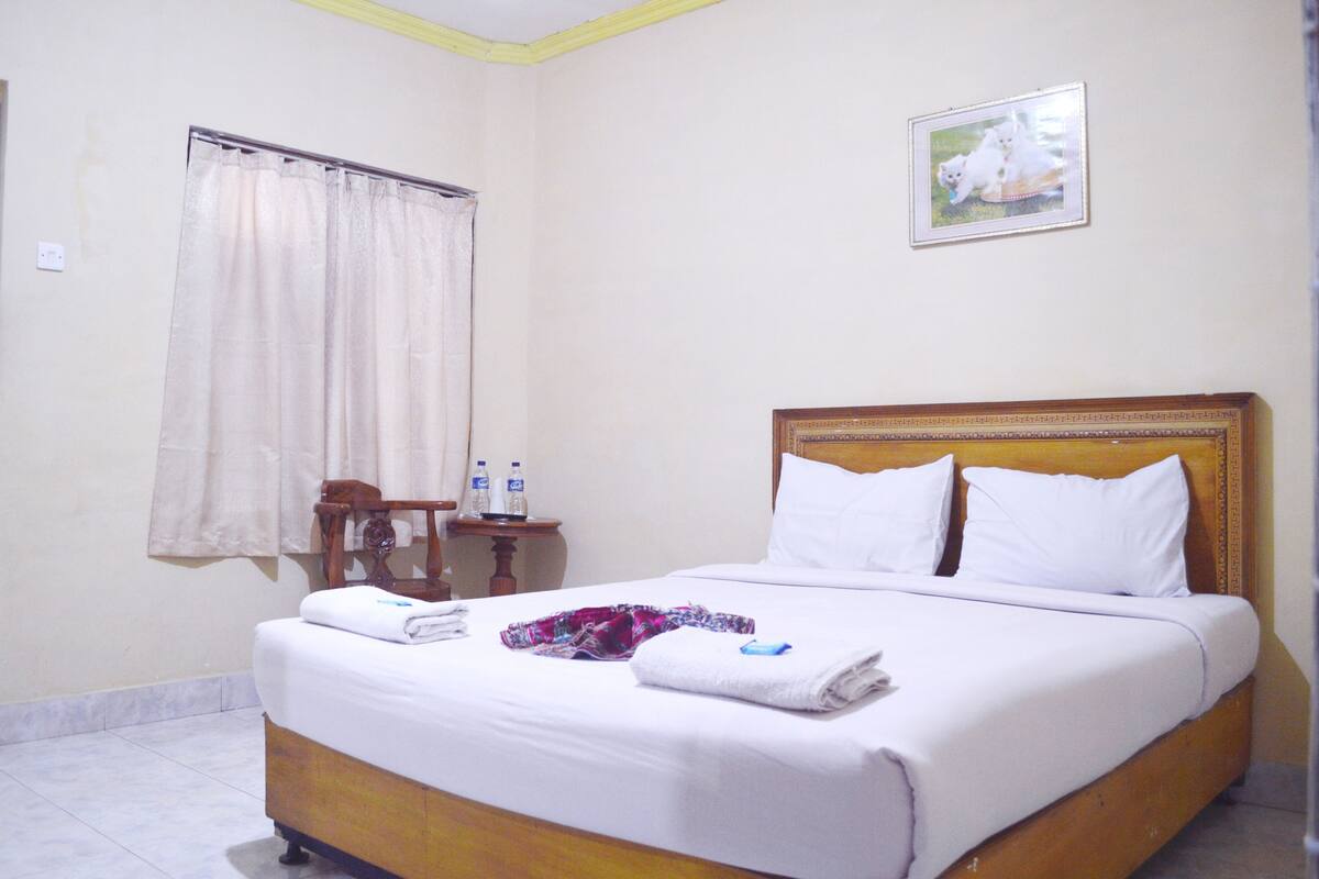 Habitación de hotel con cama, mesita de noche, ventana con cortinas e imagen en la pared.