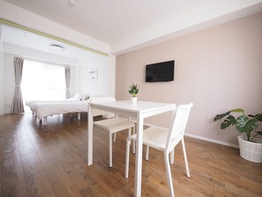 A modern, minimalist room with a wooden floor, white furniture, a flat-screen TV, and a potted plant. - Living CUBE Tabata Station (Tokyo)