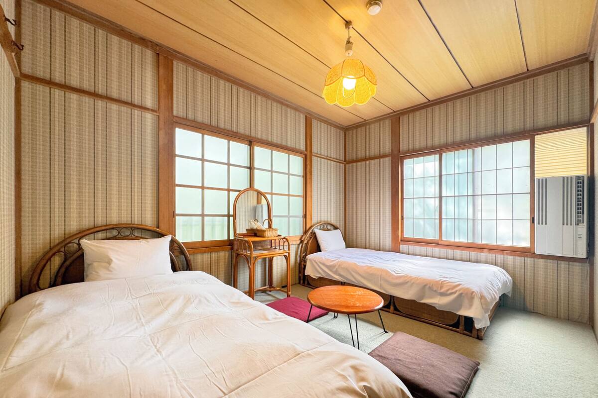 A room with two beds, a wooden ceiling, and large windows.